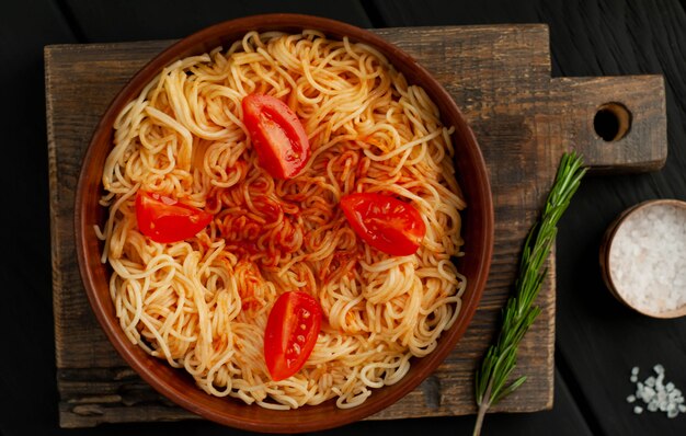 Apetyczny włoski makaron spaghetti z sosem pomidorowym, parmezan na talerzu, deska do krojenia na tle drewna. Widok z góry