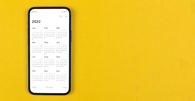 Aplikacja Kalendarz 2022 na ekranie smartfona. Obszar roboczy firmy, żółte tło. Zdjęcie w widoku z góry