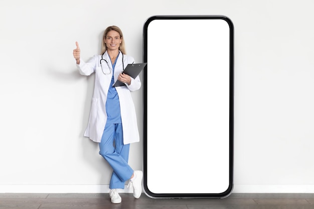 Aplikacja medyczna Uśmiechnięta pani doktor w mundurze pozowanie w pobliżu dużego pustego smartfona