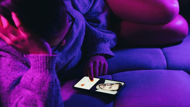 Aplikacja randkowa lub witryna randkowa na ekranie telefonu komórkowego Kobieta leży na kanapie, przesuwając i lubiąc profile na witrynie lub aplikacji dotyczącej związku Samotna kobieta korzystająca ze smartfona, aby znaleźć partnera i dziewczynę