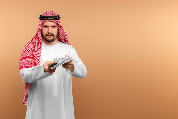 Arab biznesmen w krajowych ubraniach trzyma w rękach dolary.