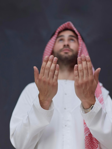 Arab w tradycyjnych strojach modlący się do Boga lub wykonujący dua. Muzułmański chłopiec trzyma ręce w pozycji modlitewnej przed czarną tablicą reprezentującą koncepcję Ramadanu