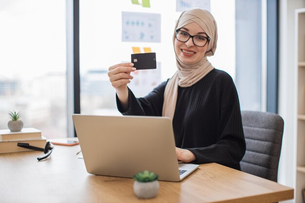 Arabka z kartą kredytową korzystająca z laptopa w miejscu pracy