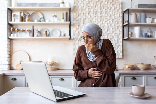 Arabska młoda kobieta w hidżabie jest w ciąży i pracuje na laptopie, czuje się źle, odczuwa silne mdłości