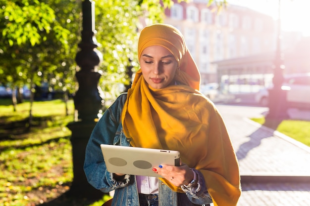 Arabska Studentka. Piękna Muzułmańska Studentka Ubrana W Jasny żółty Hidżab Trzymając Tabletkę.