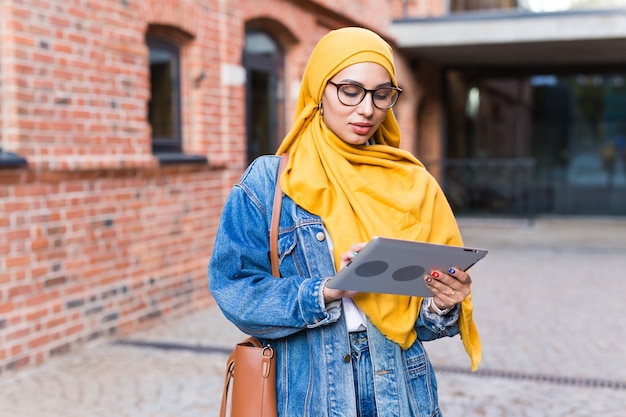 Arabska Studentka. Piękna Muzułmańska Studentka Ubrana W Jasny żółty Hidżab Trzymając Tabletkę.