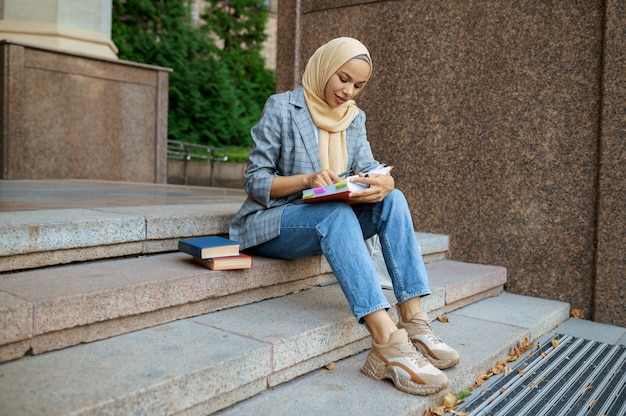 Arabska Studentka Siedzi Na Schodach Na Uniwersytecie. Muzułmanka Nakłada Makijaż Przy Wejściu Do Centrum Biznesowego.