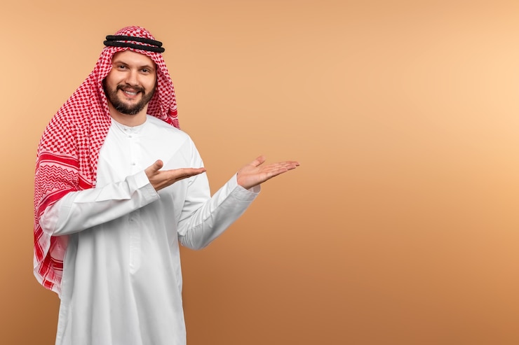 Zdjęcie arabski biznesmen w krajowych ubraniach wyświetla coś, beżową ścianę.