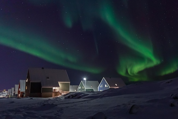 Arktyczna wioska i zielone fale zorzy polarnej nad domami Eskimosów na przedmieściach Nuuk Grenlandia
