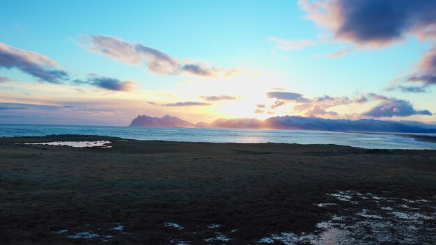 Arktyczny krajobraz czarnej piaszczystej plaży w Islandii, skandynawski krajobraz śnieżnych wzgórz i zimnej wody.