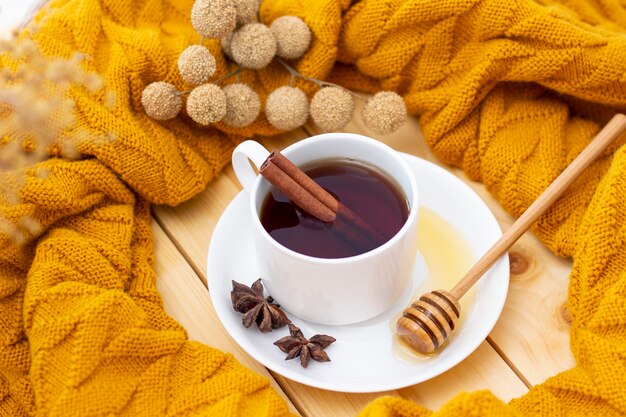 Aromatyczna gorąca cynamonowa herbata przykryta ciepłym szalikiem na drewnianym jesiennym tle. miód z miodem