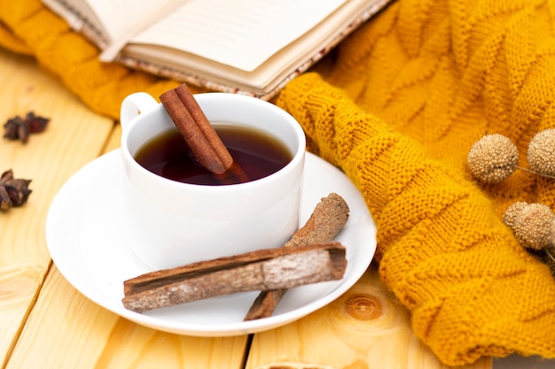 Aromatyczna Gorąca Cynamonowa Herbata Przykryta Ciepłym Szalikiem Na Drewnianym Jesiennym Tle. Wygodne Czytanie Książki.