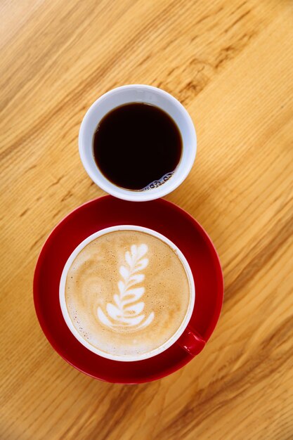 Aromatyczna kawa w czerwonej filiżance z dojną pianką i latte art oraz świeżo parzona kawa w białej filiżance o