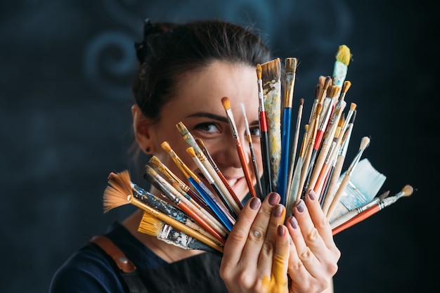 Zdjęcie artykuły artystyczne i artystyczne. narzędzia dla talentów. uśmiechnięta kobieta malarz w fartuch pozowanie z wiązką pędzli.