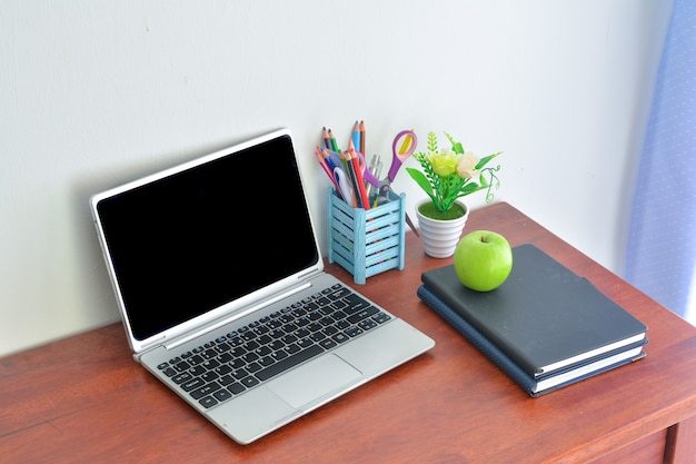 Artykuły biurowe, laptop z notatnikiem i jabłkiem na drewnianym stole