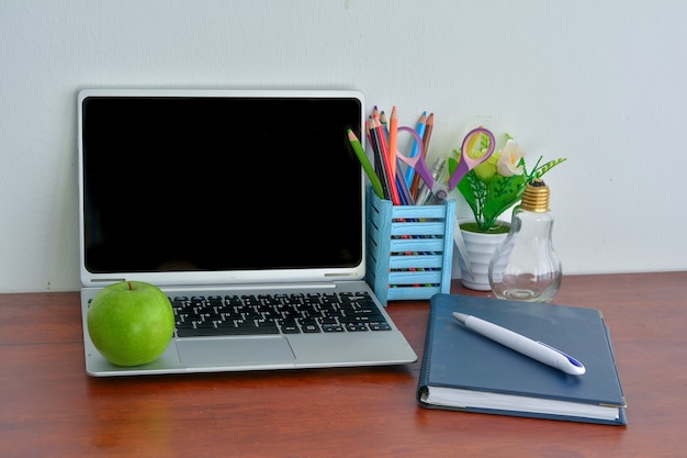 Artykuły biurowe, laptop z notatnikiem i jabłkiem na drewnianym stole