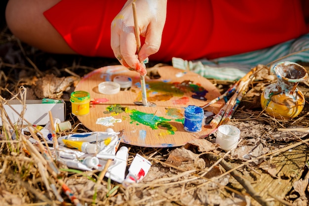 Zdjęcie artysta ręcznie rysuje obraz i paletę z farbami i pędzlami na tle trawy.