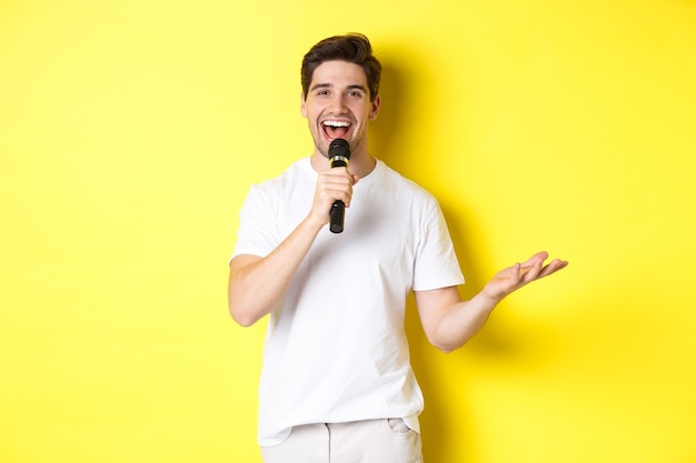 Artysta szczęśliwy człowiek występujący, mówiący do mikrofonu, wygłaszający mowę lub stand-up show, stojący na żółtym tle.