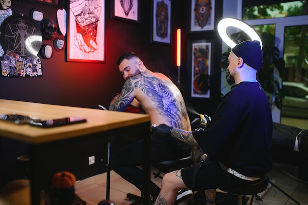 Artysta tatuażu z czarnymi rękawiczkami rysuje tatuaż rycerza na facetach z powrotem w studiu.