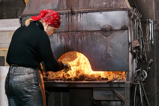 Artystka metalu podgrzewa obrabiany przedmiot w płonącym piecu kuźniczym