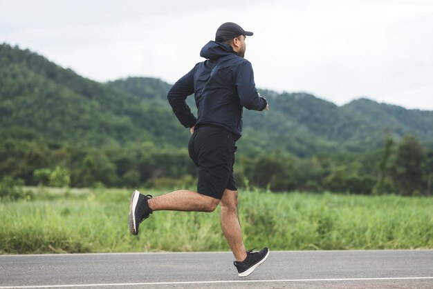 Asia człowiek ubrany sportową bieganie na drodze z górskim tłem. Młody człowiek jogging do ćwiczeń w naturze. koncepcja zdrowego stylu życia i sportu