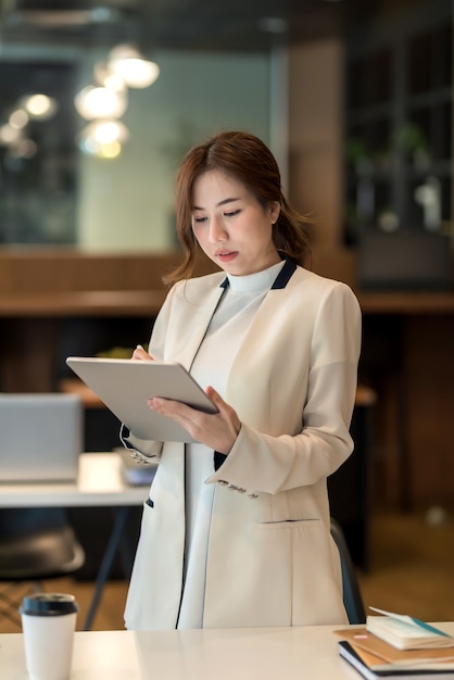 Asian Business kobieta stoi poważnie o pracy z tabletem w biurze.