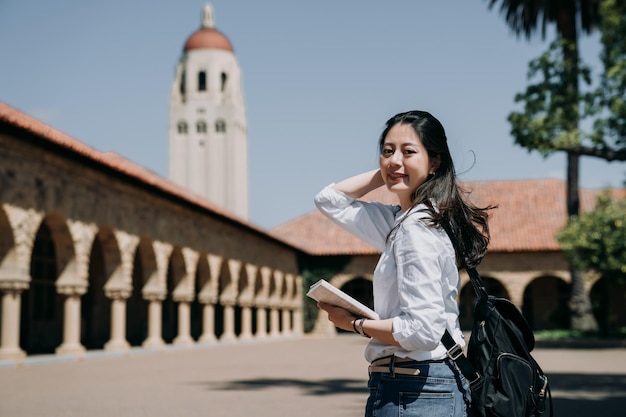 asian college girl stojący na świeżym powietrzu idzie do klasy w szkole w programie letniej trasy koncertowej. elegancka, inteligentna wymiana studentów za granicą w stanford w usa. młoda kobieta studentka pierwszego roku w nowym semestrze wesoły uśmiech