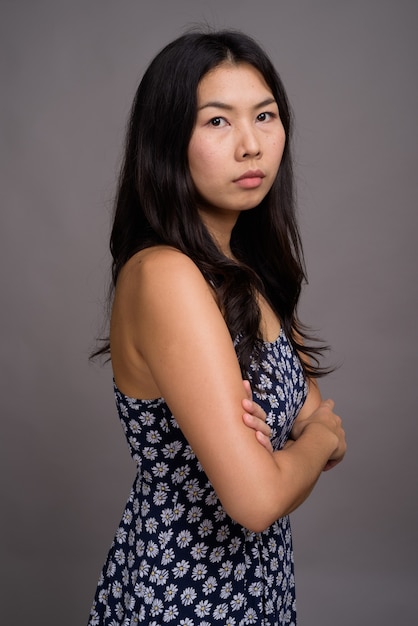 Asian kobieta ubrana w niebieską sukienkę na szarej ścianie