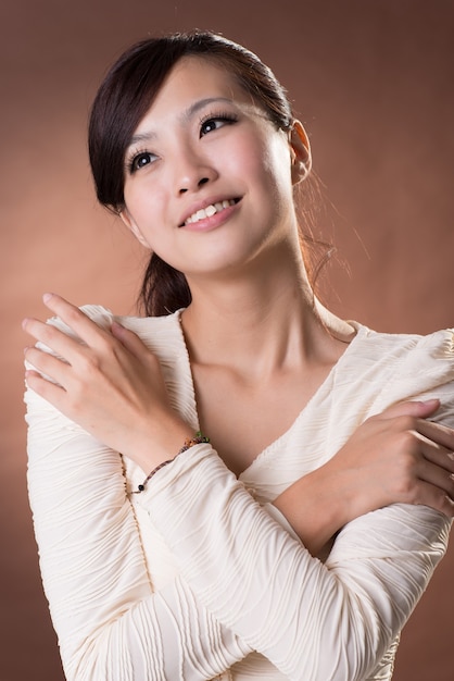 Asian młoda kobieta z wyrażeniem szczęścia, portret zbliżenie na tle studio brązowym.