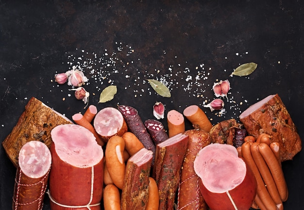 Zdjęcie asortyment produktów mięsnych, w tym kiełbasa szynka boczek przyprawy czosnek na czarnym stole widok z góry.