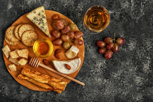Asortyment sera z winem, miodem, orzechami i winogronami na desce do krojenia.