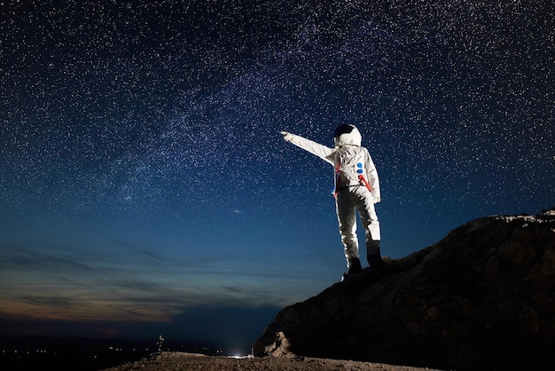 Astronauta stojący na skalistej górze pod nocnym gwiaździstym niebem