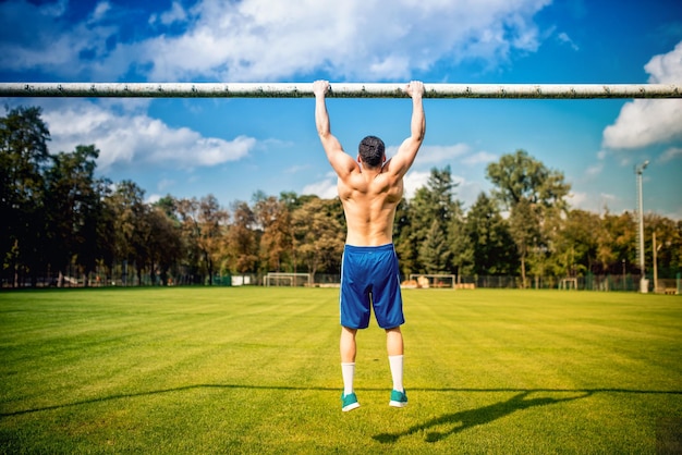 Atheltic zbudowany mężczyzna robi chinups i podstawowego szkolenia w parku Fitness piłkarz szkolenia