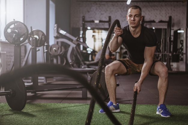 Atleta crossfit męski pracujący z batalistycznymi arkanami przy gym