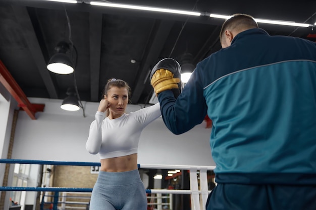 Atletyczna kobieta uderza męskiego trenera na lekcji taebo w siłowni