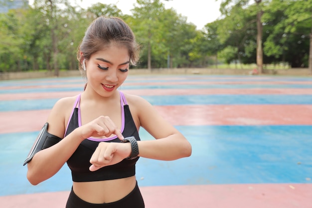 Atletyczna młoda zdrowa azjatycka kobieta w sportowej pozycji stojącej i korzystająca z urządzenia śledzącego fitness na inteligentnym zegarku po rozciągnięciu na świeżym powietrzu na poranne ćwiczenia. Koncepcja sportu i technologii