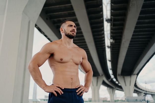 Atletyczny męski model fitness pozuje z muskularnym ciałem skoncentrowanym na świeżym powietrzu Regularne ćwiczenia sportowe dla aktywnego stylu życia