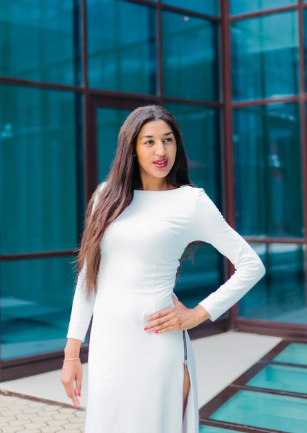 Atrakcyjna afro kobieta w luksusowej białej sukni na tle budynku z niebieskimi oknami