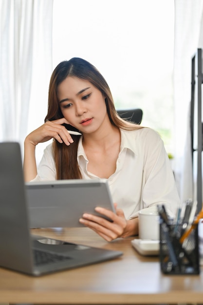 Atrakcyjna azjatycka bizneswoman pracująca przy biurku przy użyciu cyfrowego tabletu