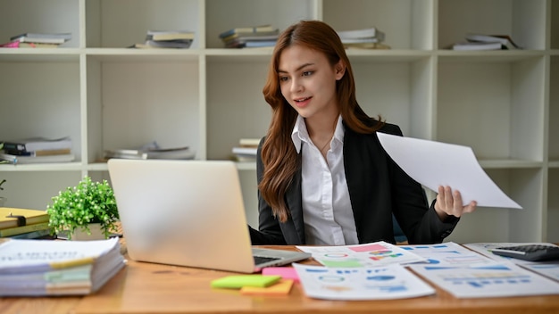 Atrakcyjna azjatycka bizneswoman pracuje nad swoimi raportami finansowymi przy biurku w biurze