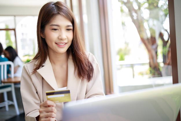 Atrakcyjna azjatycka bizneswoman używająca karty kredytowej do płatności za towary zakupy online przez laptop w kawiarni Pewna i inteligentna kobieta oraz koncepcja biznesowa