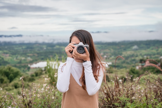 Atrakcyjna azjatycka kobieta robi zdjęcie z retro kamerą filmową wśród przyrody na wsi rano