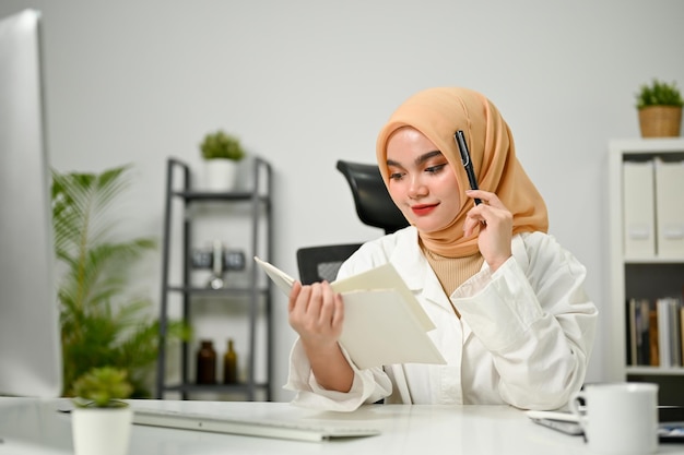 Atrakcyjna azjatycka muzułmańska bizneswoman czytająca informacje o książce przy biurku