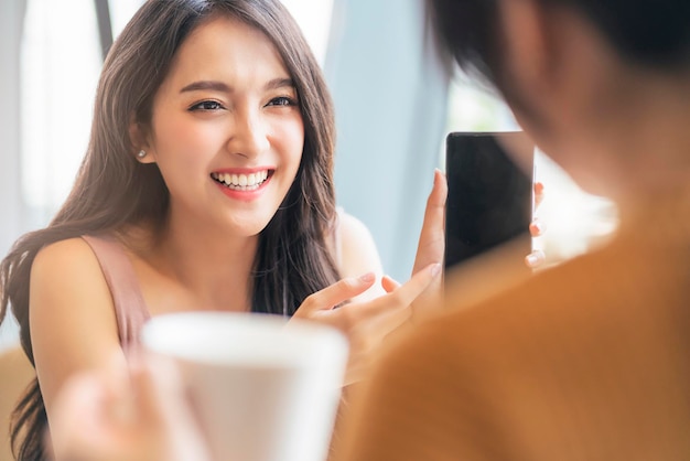 Atrakcyjna azjatycka pozytywna rozmowa o kobiecym szczęściu uśmiechnięta śmiech wesoła rozmowa z przyjacielem w kawiarni restauracji z naturalnym światłem z okna koncepcja swobodnego stylu życia