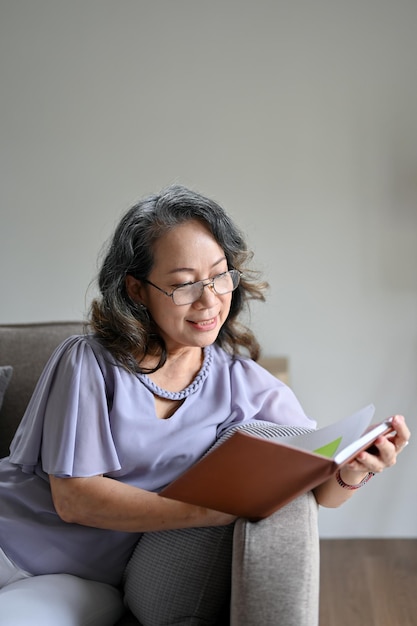 Atrakcyjna Azjatycka starsza kobieta w okularach, czytająca powieść