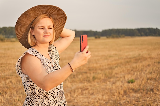 Atrakcyjna biała europejska kobieta w sukience i kapeluszu robi selfie wieczorem na świeżym powietrzu