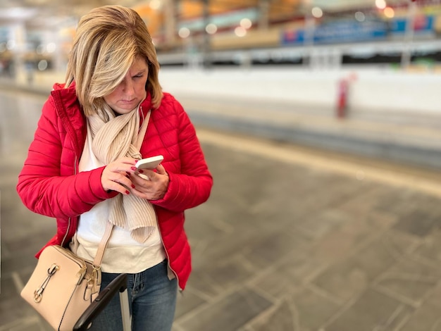 Atrakcyjna blondynka czeka na stację kolejową za pomocą telefonu komórkowego