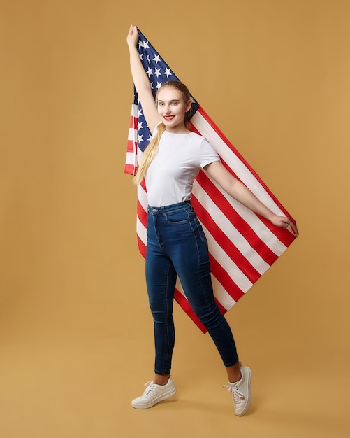 Atrakcyjna Blondynka Dumnie Pozuje Z Amerykańską Flagą. Sesja Zdjęciowa W Studio Na żółtym Tle.