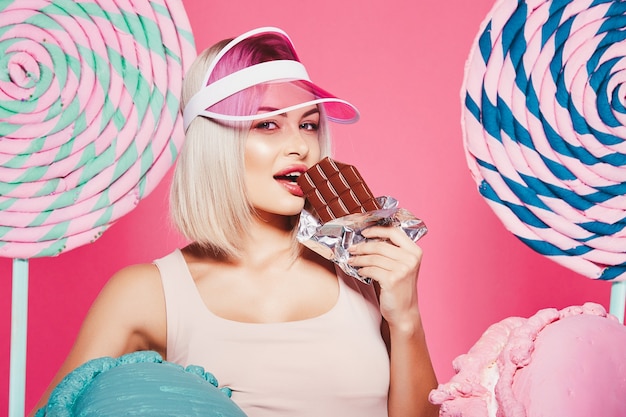 Atrakcyjna blondynka na sobie top stojący z ogromnymi słodkimi lizakami w różowym studio