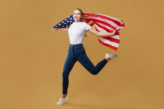 Atrakcyjna blondynka podskoczyła z amerykańską flagą. sesja zdjęciowa w studio na żółtym tle.